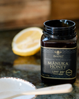 BeeNZ Manuka Honey umf20+ jar on a countertop with a spoon and lemon in the background