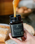 Manuka honey being spooned from a jar with bread in the background
