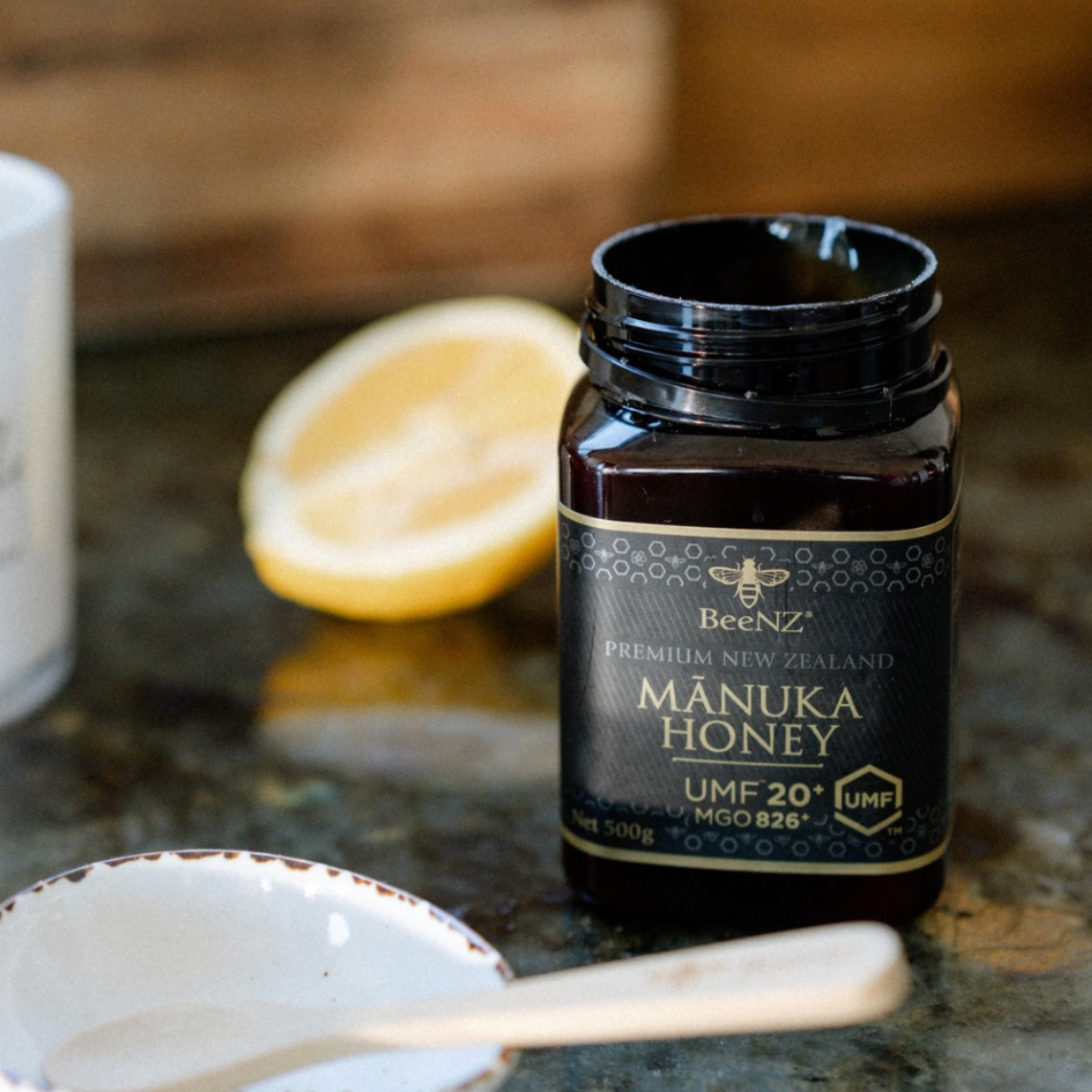 BeeNZ Manuka Honey umf20+ jar on a countertop with a spoon and lemon in the background