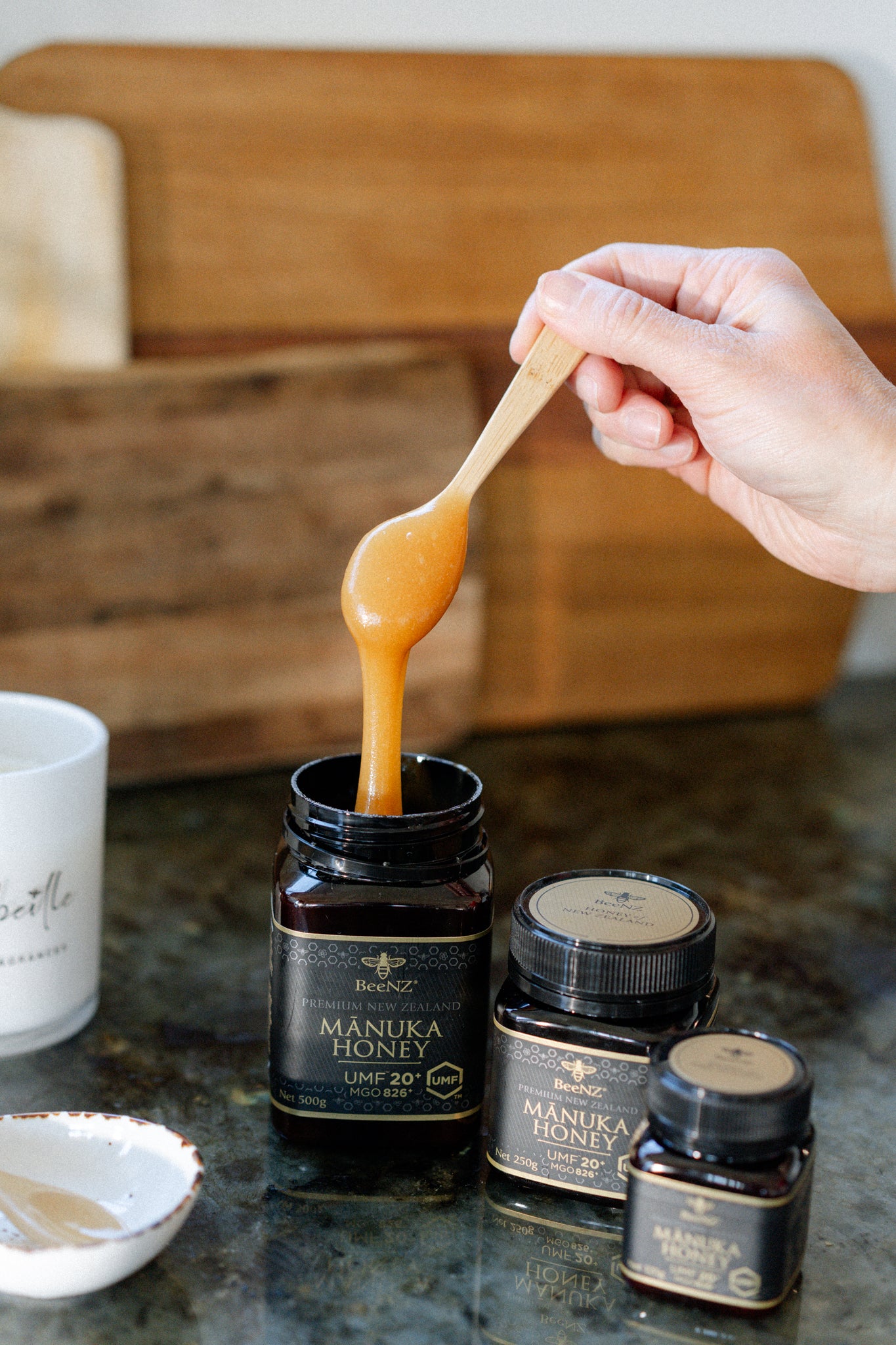Manuka honey being scooped with a spoon from a jar on a kitchen counter.